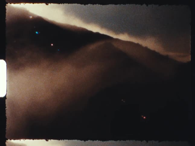 An atmospheric 8mm film shot of fog slowly moving over a dark mountain range
