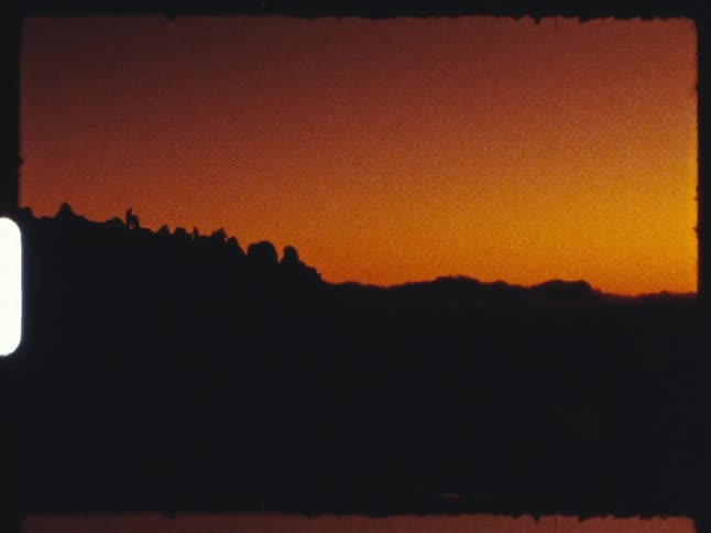 An 8mm film shows the silhouette of a mountain range against a vibrant orange sunset, ending with a white film burn