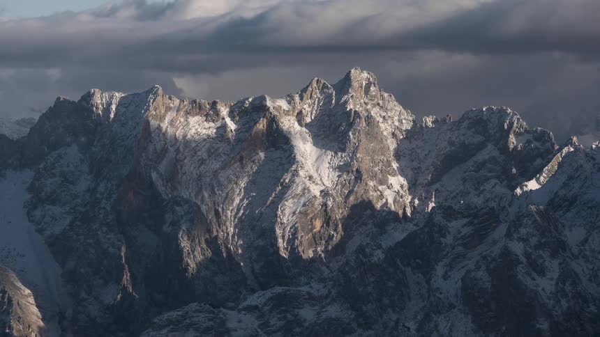 A slow, dramatic zoom out reveals a vast, majestic mountain range covered in snow under a cloudy sky