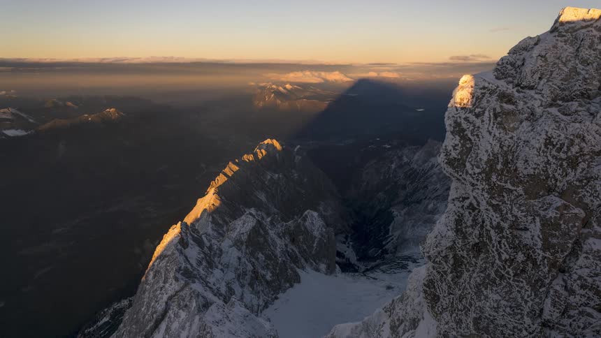 A majestic sunrise time-lapse from a high, snowy mountain peak shows its shadow moving across the vast valley and distant ranges
