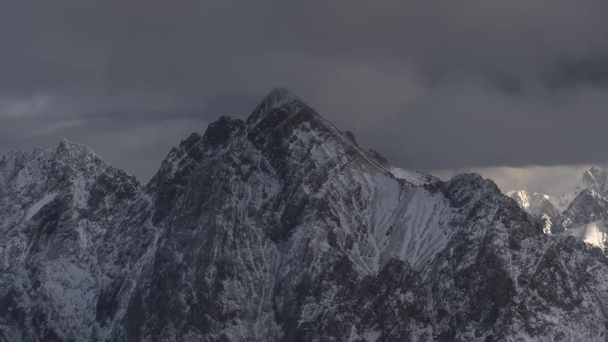 Timelapse of dramatic dark clouds engulfing a sunlit snow-capped mountain peak