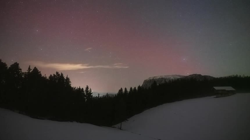 A stunning timelapse of the Aurora Borealis painting the night sky with pink and green hues over a tranquil snowy mountain landscape