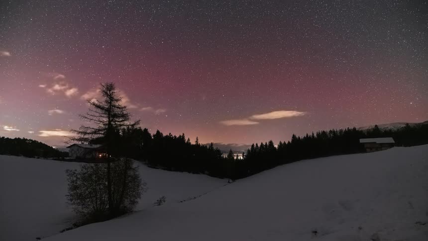 Stunning time-lapse captures the magenta hues of the Aurora Borealis and moving clouds across a star-filled sky over a snowy forest landscape