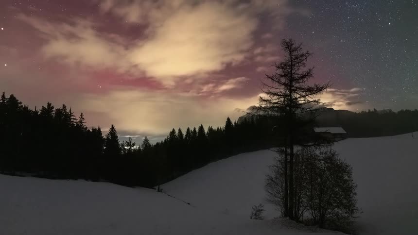 A mesmerizing timelapse of fog and clouds clearing over a snowy mountain landscape at night to reveal a spectacular starry sky with a colorful Aurora Borealis