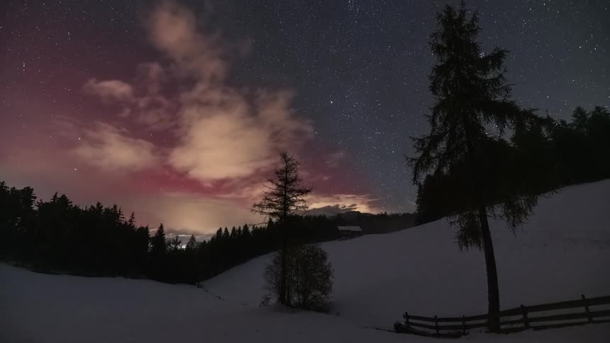 Stunning time-lapse captures the vibrant red Aurora Borealis dancing in the starry night sky over a serene, snow-covered forest