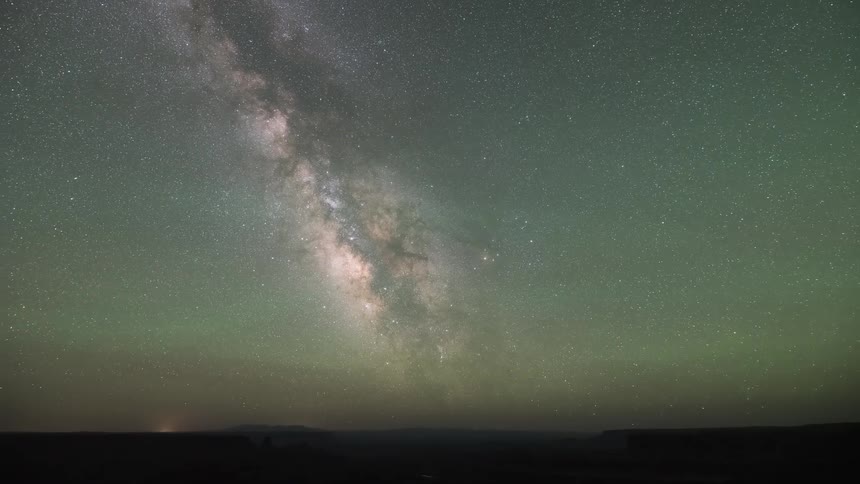 A stunning time-lapse captures the Milky Way galaxy and countless stars moving across the night sky, with a faint green airglow visible above the dark horizon