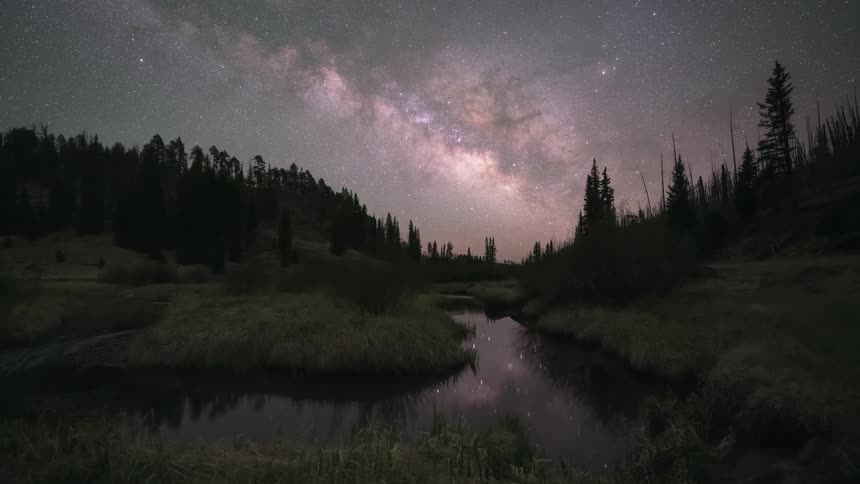 A breathtaking timelapse captures the transition from twilight to a star-filled night as the Milky Way rises over a serene mountain river