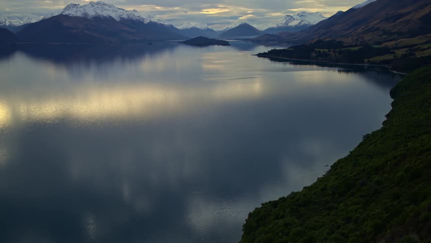A slow tilt up reveals a serene lake reflecting the beautiful snow-capped mountains of New Zealand at dusk