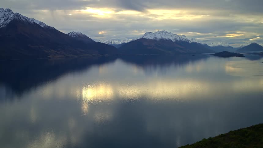 A slow zoom out reveals the breathtaking scenery of a serene mountain lake reflecting snow-capped peaks at dusk