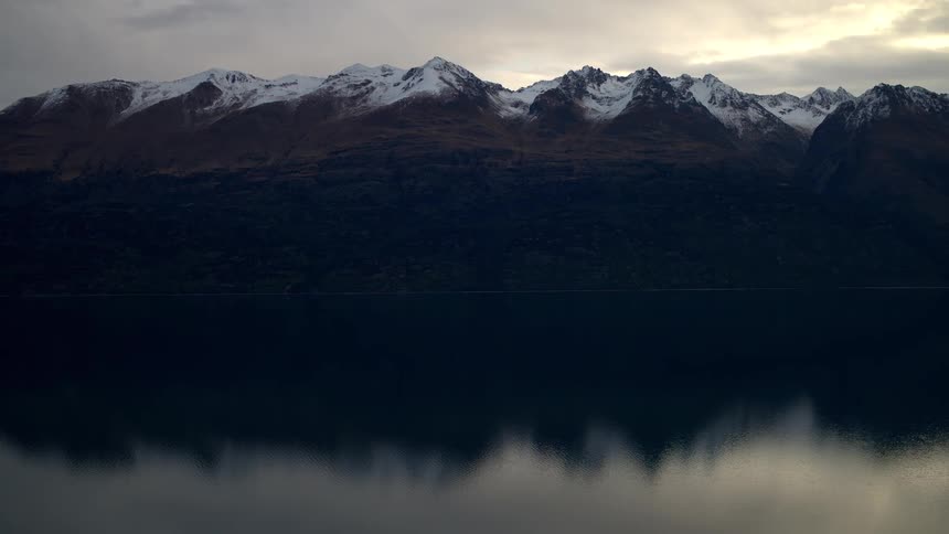 A tranquil wide shot captures the majestic snow-capped mountains reflecting perfectly in the serene, still lake below