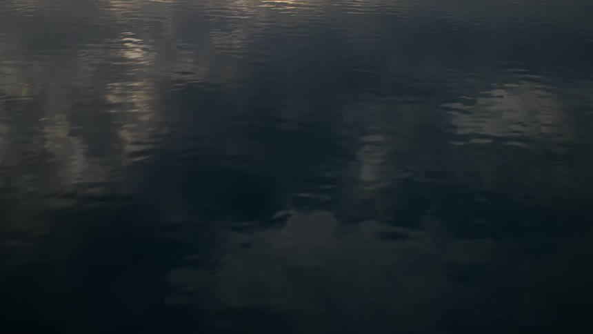 A slow camera tilt up reveals a breathtaking view of a serene mountain lake reflecting the snow-capped peaks and a dramatic cloudy sky at sunrise
