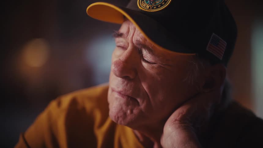 A close-up shot of a pensive elderly U.S. Army veteran in a hat, solemnly lost in thought