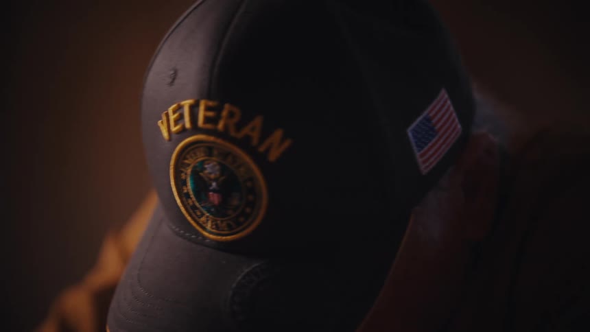 A solemn close-up shot of a U.S. Army veteran's hat as he looks down in reflection