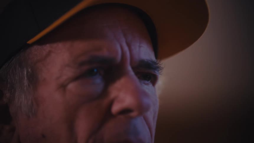 An elderly United States Army veteran removes his glasses, revealing a somber and emotional expression in a slow-motion close-up