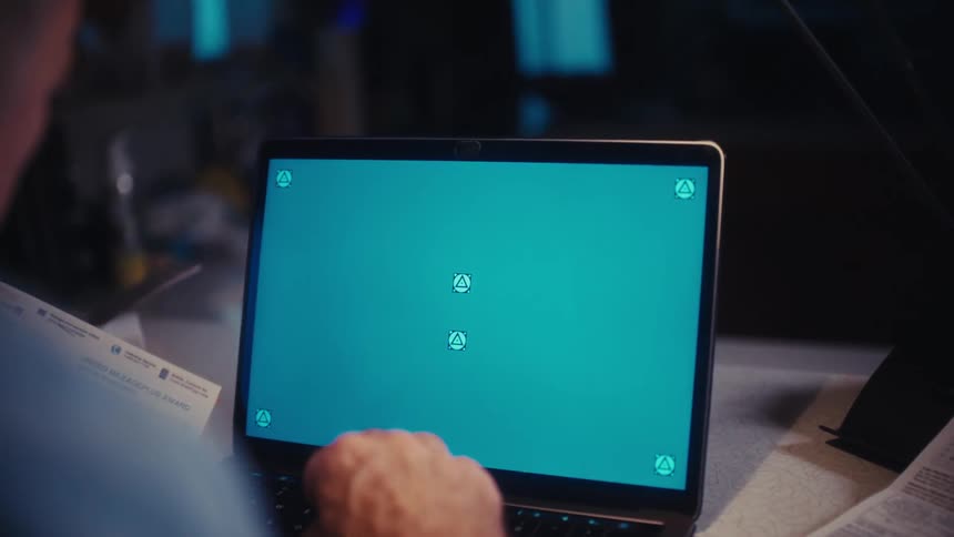 An over-the-shoulder shot of a person reviewing paperwork while sitting in front of a green screen laptop at a desk in a dark room