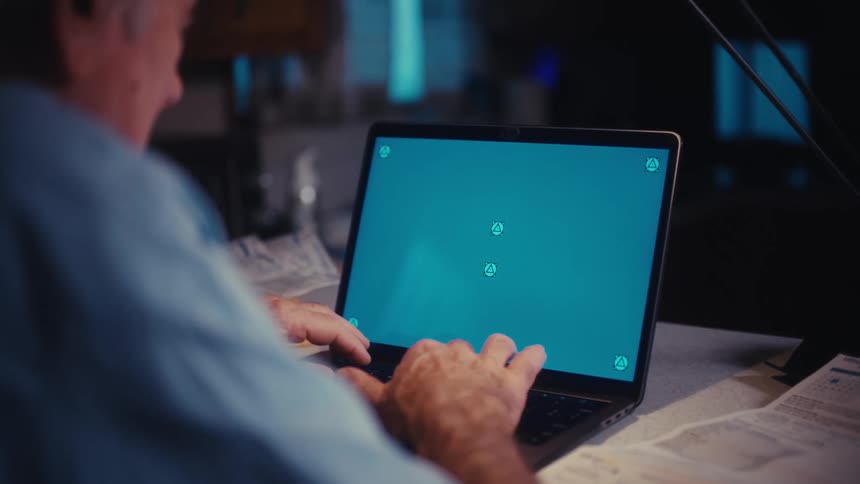 Over the shoulder shot of an elderly man typing on a laptop computer with a green screen