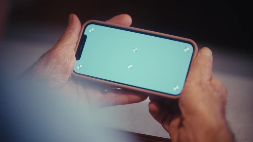 An elderly person holds a smartphone with a blank chroma key screen ready for content