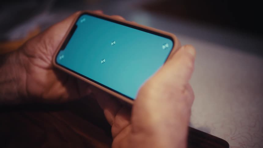 A close-up over-the-shoulder shot of a person holding a smartphone horizontally with a trackable chroma key screen
