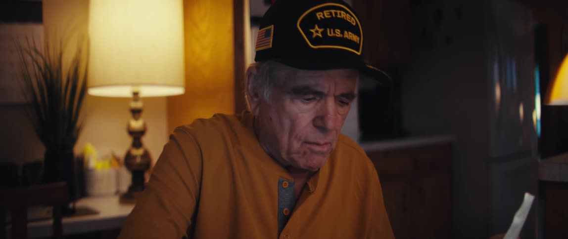 An elderly retired U.S. Army veteran looks worried as he calculates his bills and receipts at a table in his home