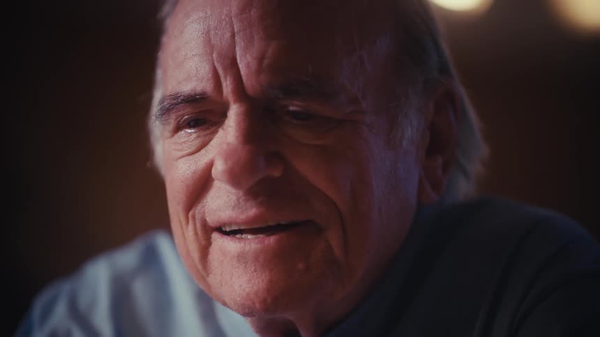 Rack focus from an elderly man's hands on a smartphone to his face as he bursts into a happy laugh