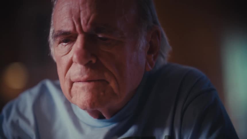 An elderly Army veteran becomes emotional and smiles with a tear in his eye while using his smartphone at night