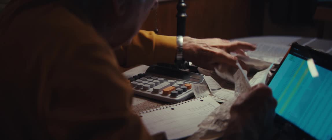 An elderly veteran with a concerned expression meticulously sorts through receipts and bills to manage his finances at night