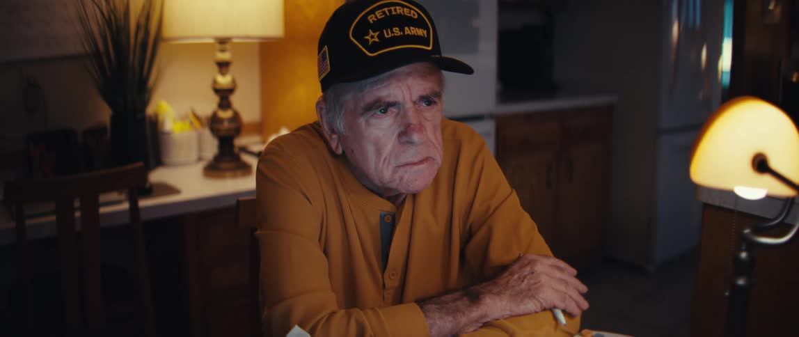 A worried, elderly U.S. Army veteran sits at his dimly lit kitchen table at night, stressed about his finances and bills