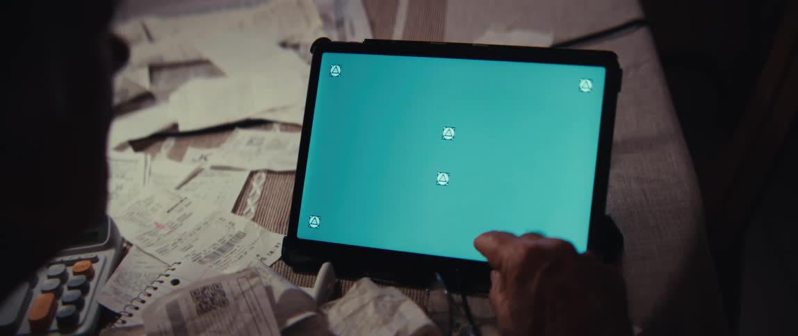 An over-the-shoulder view of a person tapping on a green screen tablet while surrounded by paperwork and receipts
