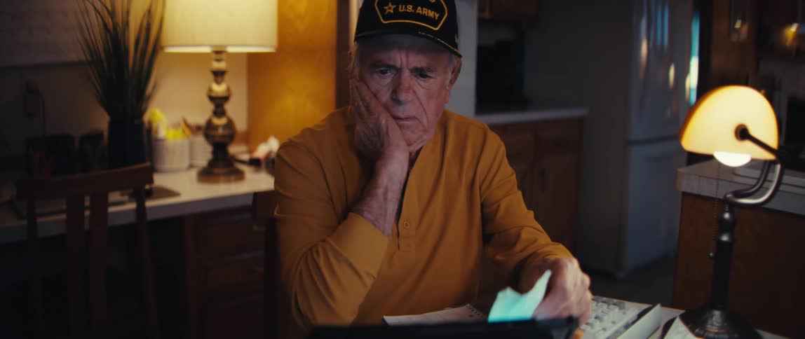A retired U.S. Army veteran looks worried and stressed while calculating his bills and finances on a tablet at his kitchen table late at night