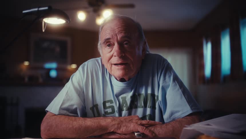 An elderly U.S. Army veteran takes a moment from his work, closes his laptop, and offers a proud, reflective look to the camera