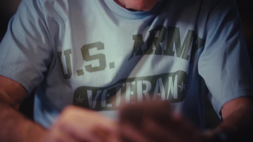 A happy elderly US Army veteran smiles while scrolling on his smartphone at home