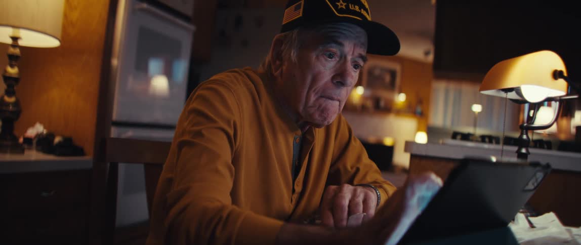 A retired US Army veteran scrolls through his tablet in his warmly lit home, his expression changing from concentration to a heartfelt smile