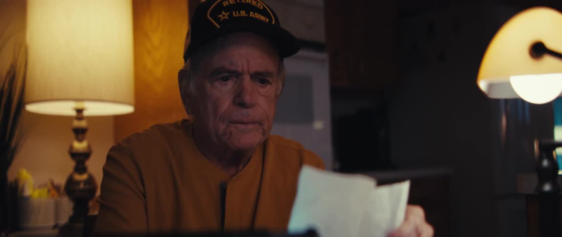 A worried elderly retired US Army veteran sits at his desk late at night, sorting through a large pile of receipts and bills