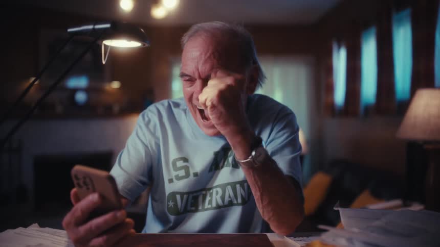 An overjoyed elderly U.S. Army veteran laughs and celebrates while on a video call on his smartphone in his home