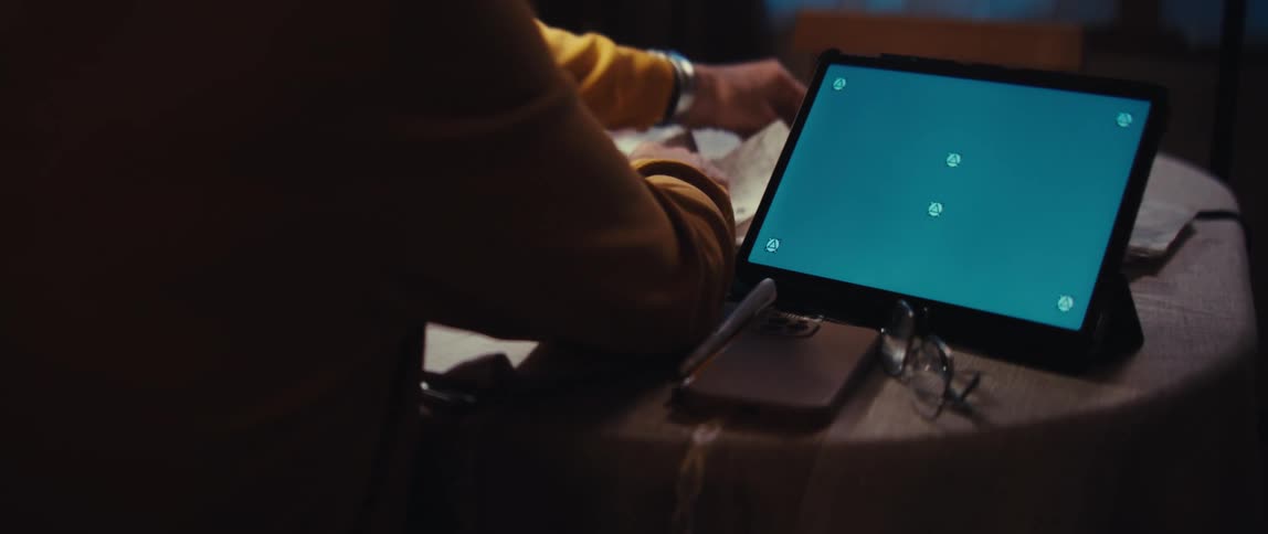 Over the shoulder shot of a person sitting at a table with a tablet featuring a green screen for compositing