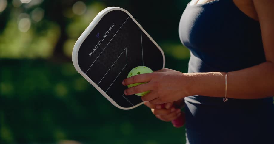 A woman holds her pickleball paddle and ball in a stylistic slow-motion shot on a sunny day