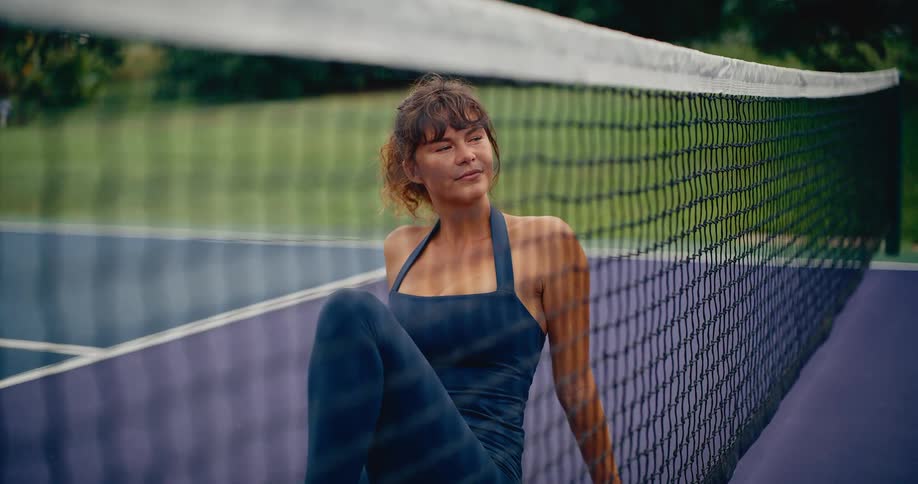 A beautiful woman in sportswear relaxes on a purple tennis court after a workout