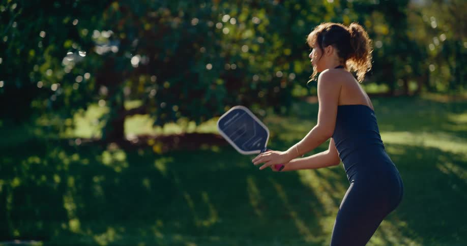A woman in athletic wear hits a pickleball in slow motion during a sunny day on an outdoor court