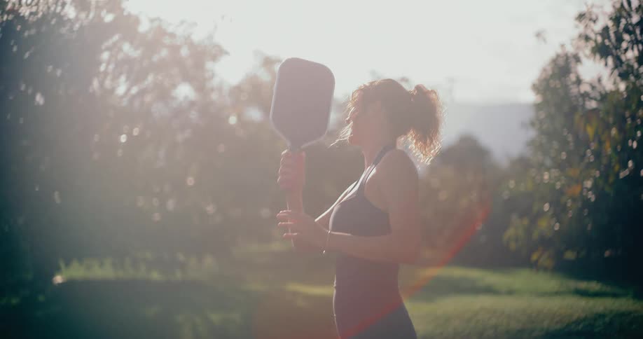 A happy woman in athletic wear playing pickleball in slow motion on a sunny day in a park