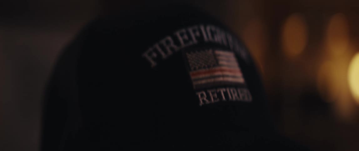 Close-up rack focus on a 'Retired Firefighter' hat with a thin red line American flag