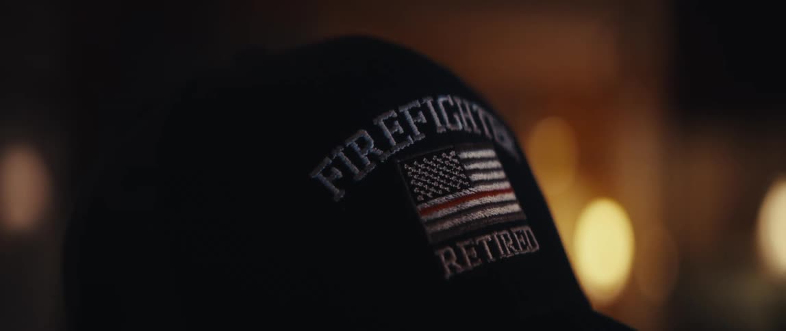 A close-up of a retired firefighter's hat featuring a thin red line American flag sits in a warmly lit room