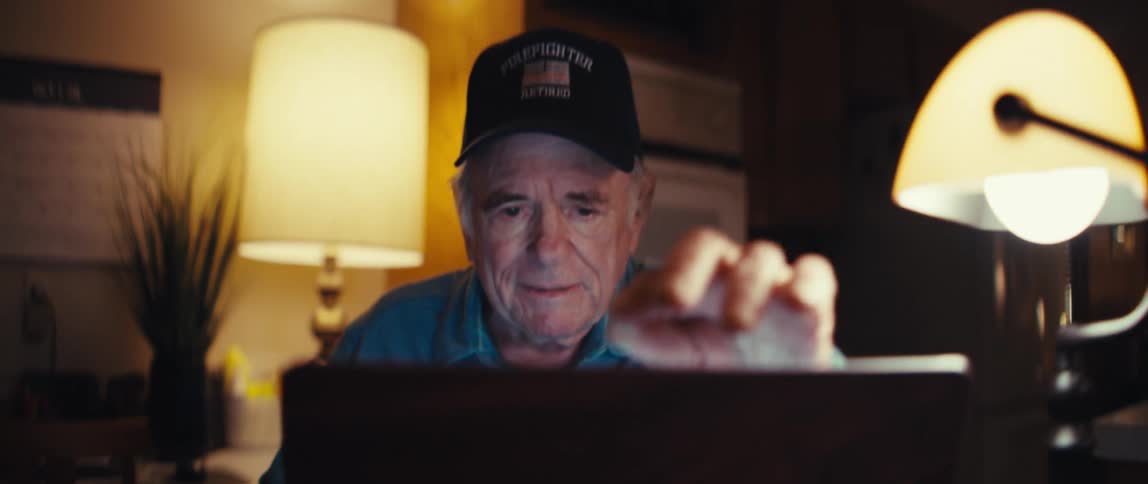 A retired firefighter smiles warmly as he opens his laptop at home in the evening