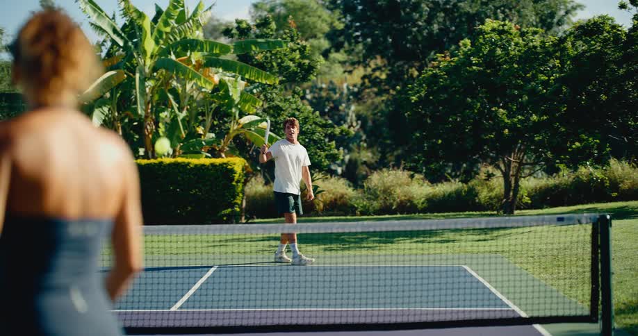 A young couple rallies back and forth while playing pickleball in slow motion on a beautiful sunny day