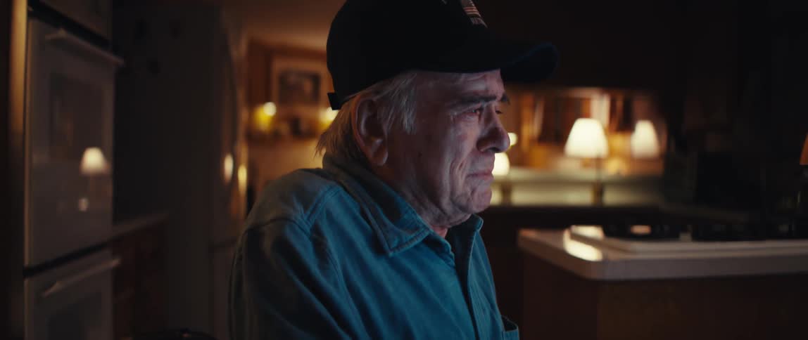 A close-up of a sad and emotional elderly retired firefighter sitting alone in his dimly lit kitchen at night