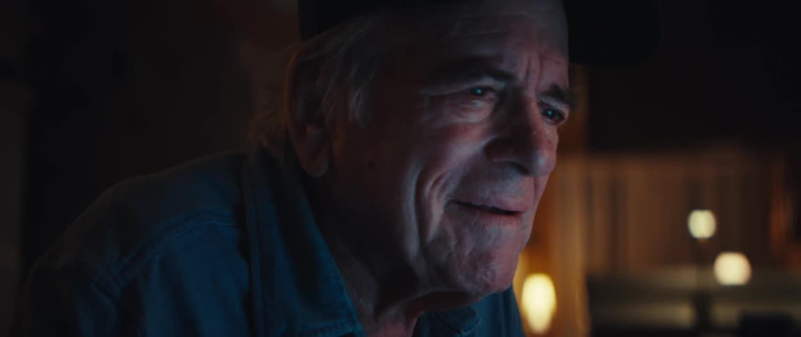 Heartwarming close-up of a senior man's face lighting up with a smile as he browses his laptop at night