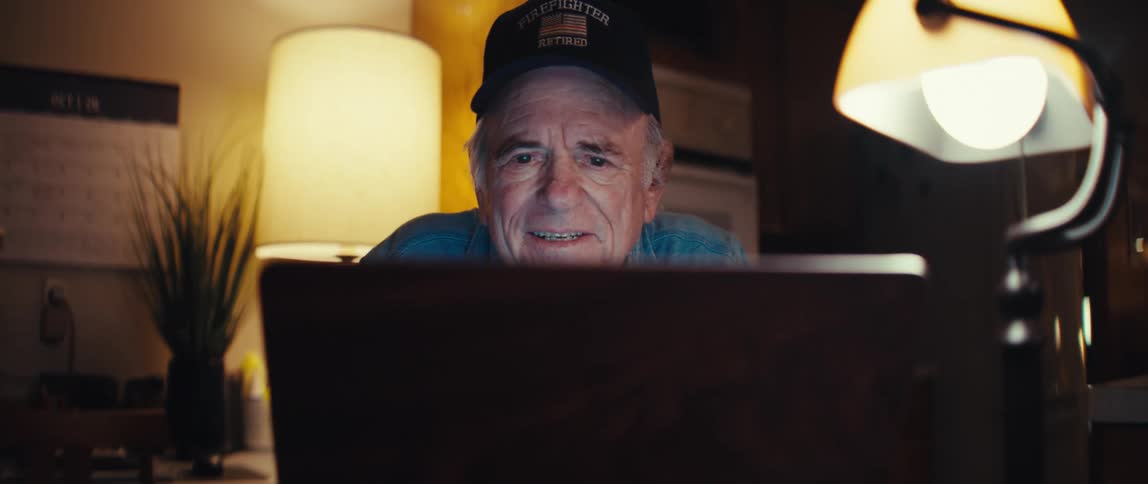 A retired firefighter's face lights up with a warm smile as he uses his laptop to connect with loved ones at night