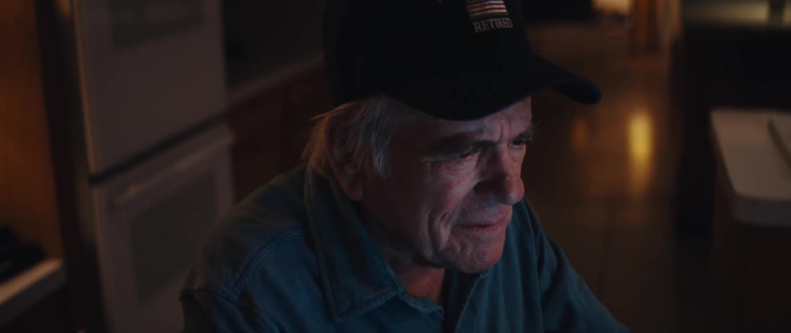 An elderly retired firefighter smiles warmly while typing on his laptop late at night in his home
