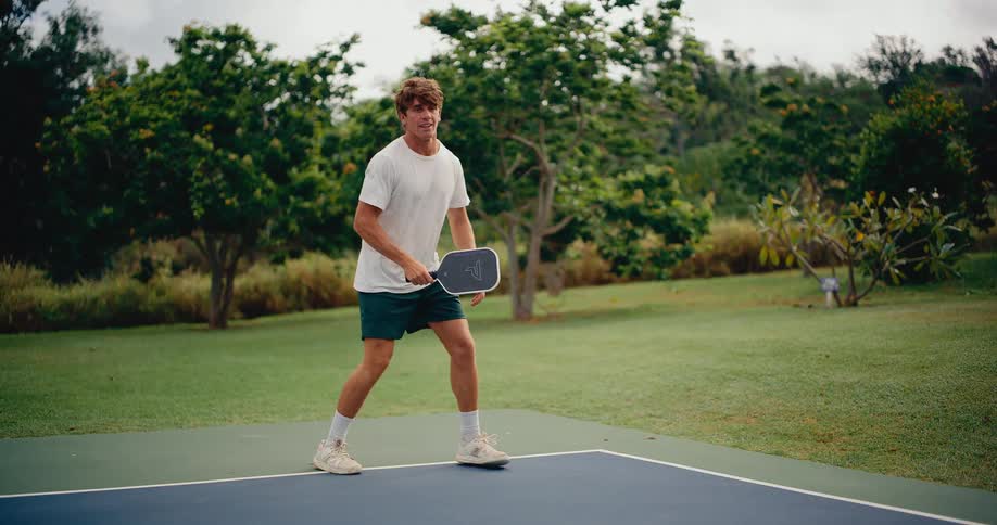 Slow motion footage shows a handsome young man skillfully playing a game of pickleball on a beautiful outdoor court