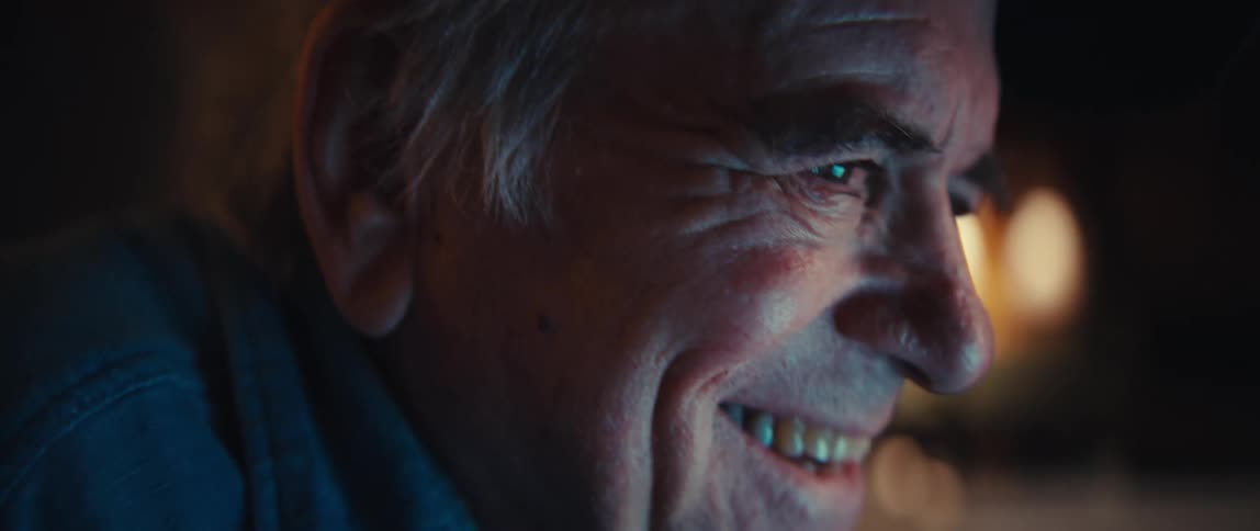 Close up on a happy elderly man smiling as he types on a laptop keyboard at night
