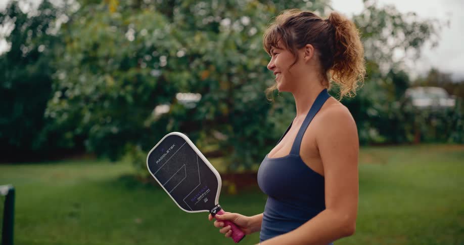 A smiling woman runs across a pickleball court holding a paddle in slow motion